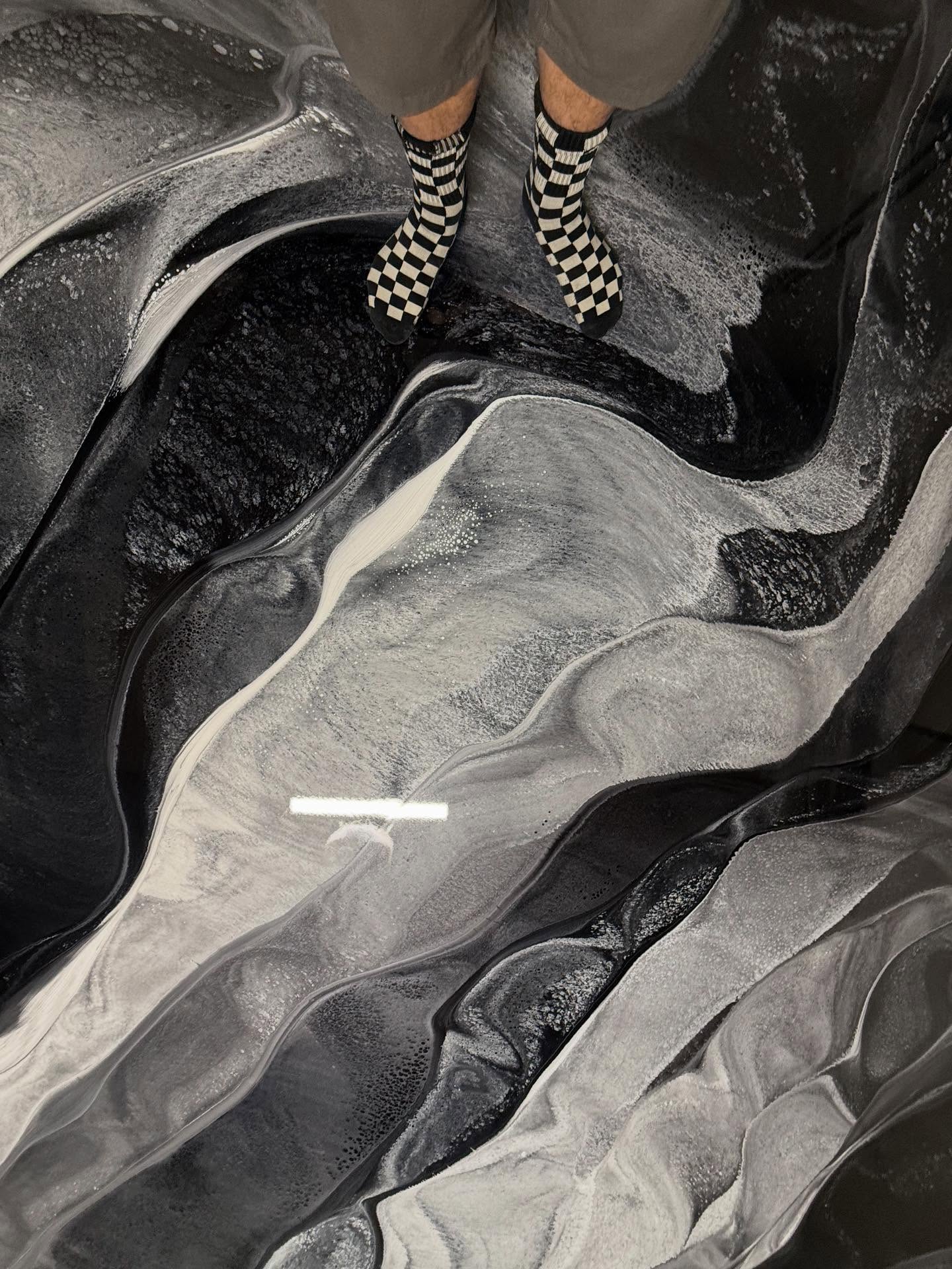 Person standing on freshly poured black and silver metallic epoxy floor in a Los Angeles residential garage, scale shot showing reflective depth